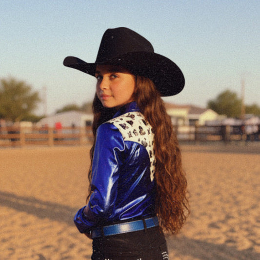 Girl wearing an electric blue western rodeo shirt with a royal flush pattern and a black cowboy hat in an outdoor setting.