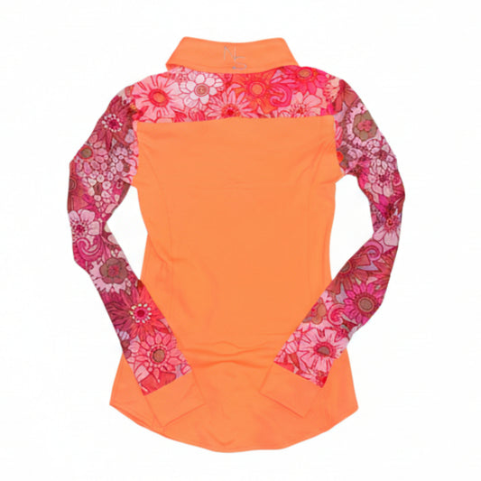 A girl wearing a retro pink and coral orange floral mesh sleeve rodeo shirt, purple pants, and a purple cowboy hat in a dirt area with buildings in the background showing the back of the shirt.