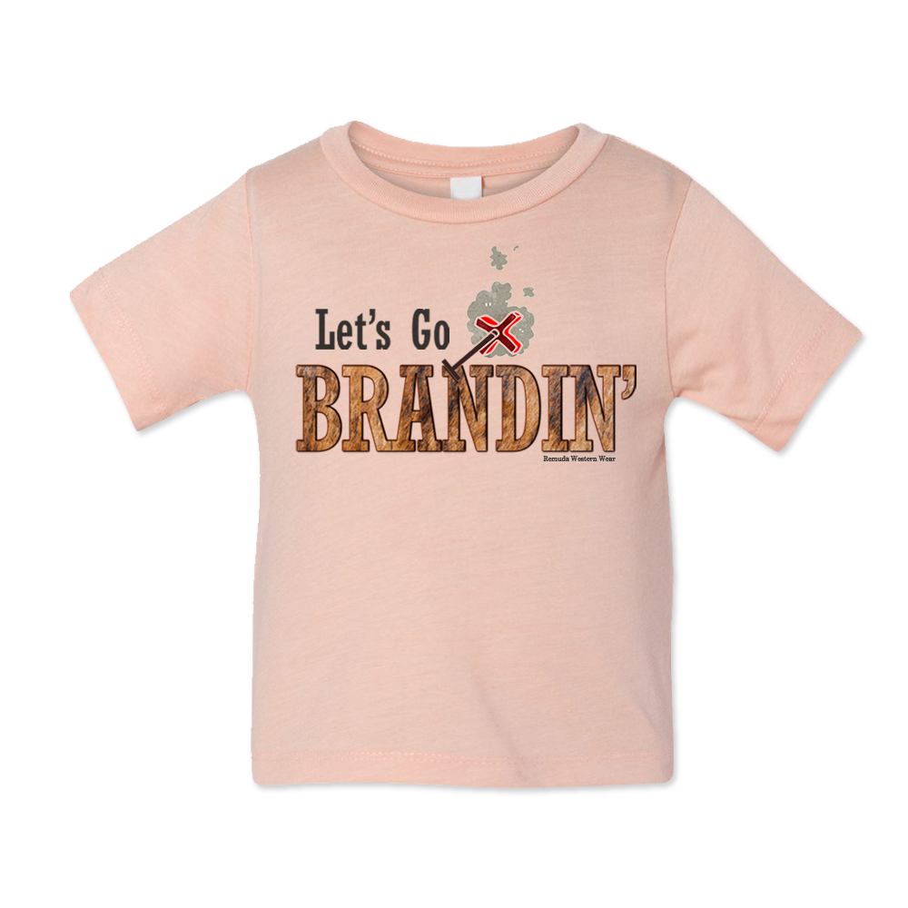 A stylish western-themed peach colored infant t-shirt featuring the phrase 'Let's Go Brandin'' prominently printed in bold, weathered letters across the chest. Above the shirt is is an illustration of a branding iron, evoking a rustic cowboy aesthetic. Kids Western wear, Ranch wear and Rodeo wear.