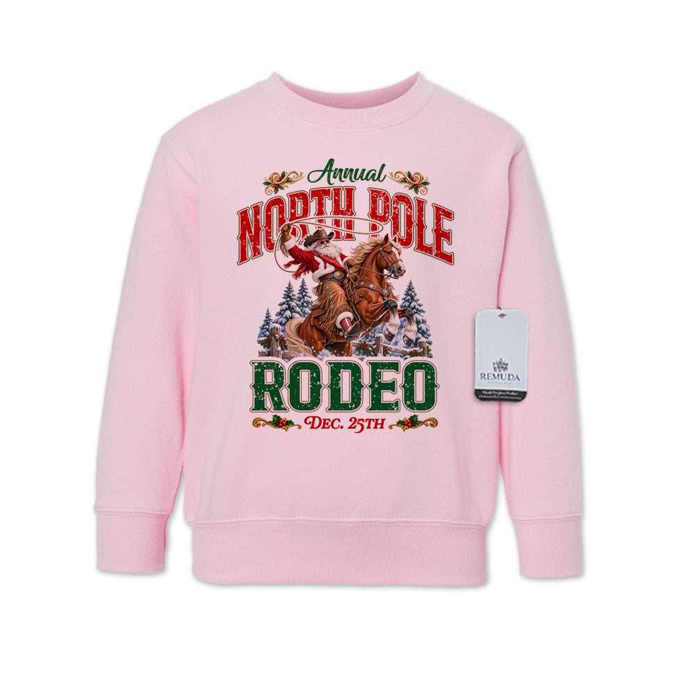 Pink toddler crewneck fleece sweatshirt featuring a festive North Pole Rodeo Christmas design with Cowboy Santa riding a rearing horse, snowy pine trees, vintage red and green lettering, December 25th details, and ribbed cuffs and hem.