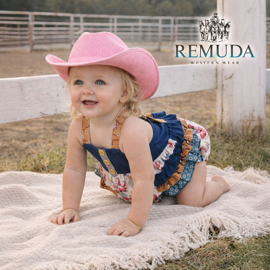 Western baby "Petals & Ponies" romper featuring a navy bodice, floral print, crossed back straps, ruffled side panels with running horses detail.