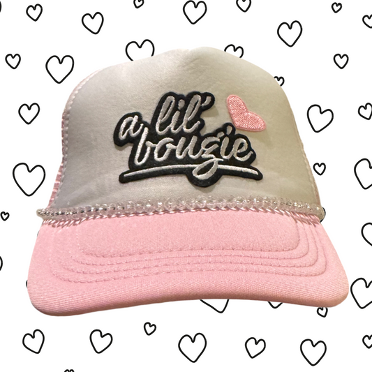 Pink and beige trucker hat with 'a lil bougie' text and heart design on a white background with hearts