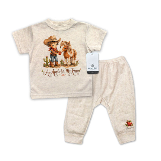 Oatmeal colored children's pajamas shirt and pants set with cowboy and horse design and an apple design on the pants on a white background