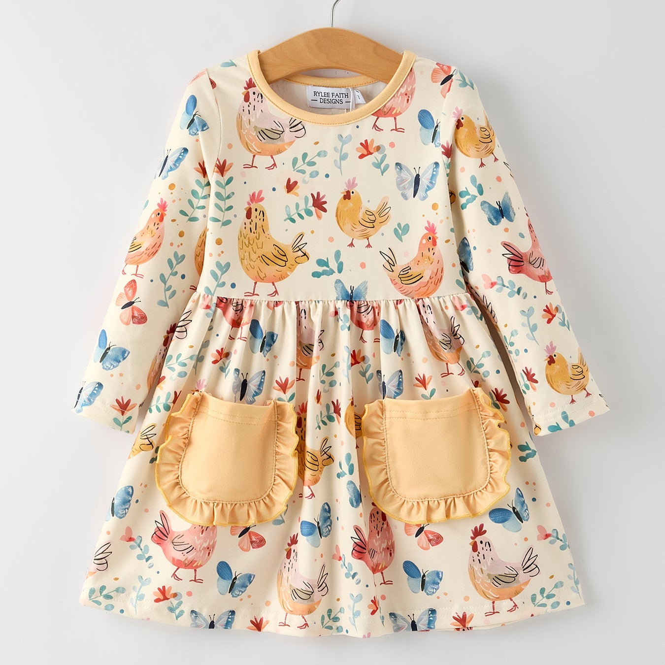 Children's dress with chicken and Butterfly pattern and yellow pockets on a hanger against a light gray background