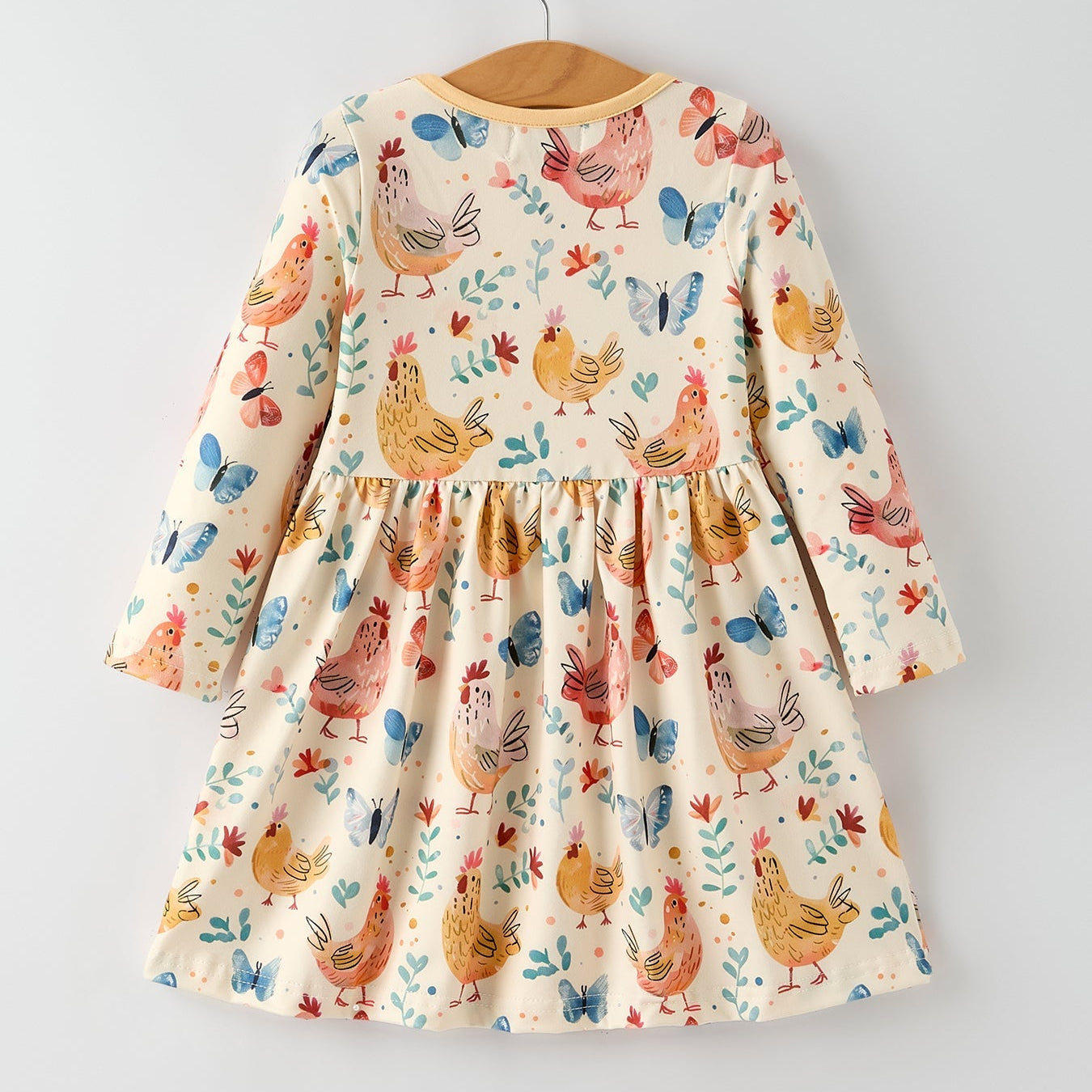 Children's dress with chicken and butterfly pattern on a hanger against a light gray background