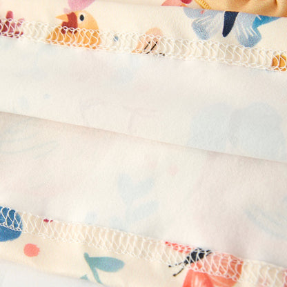 Close-up hem of a girls yellow dress with colorful chicken and butterfly designs on a light background