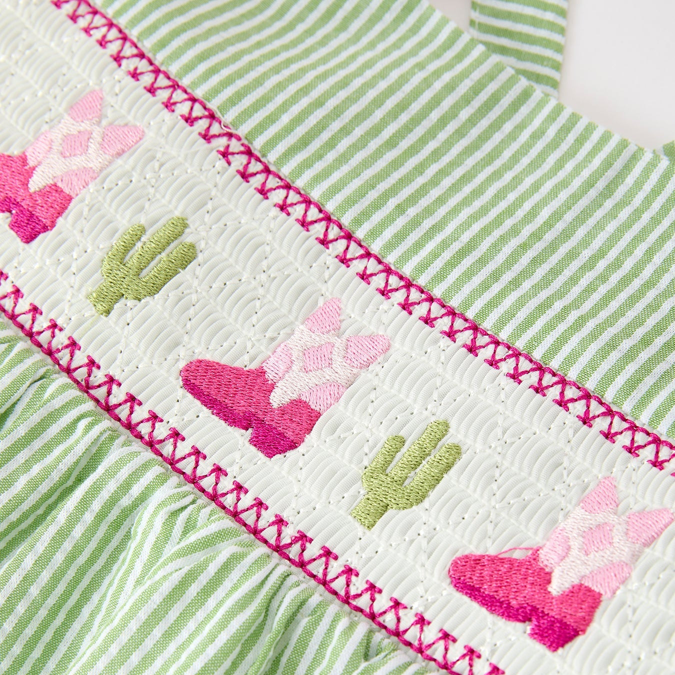 Green and white striped fabric with embroidered pink western boots and green cacti patterns.