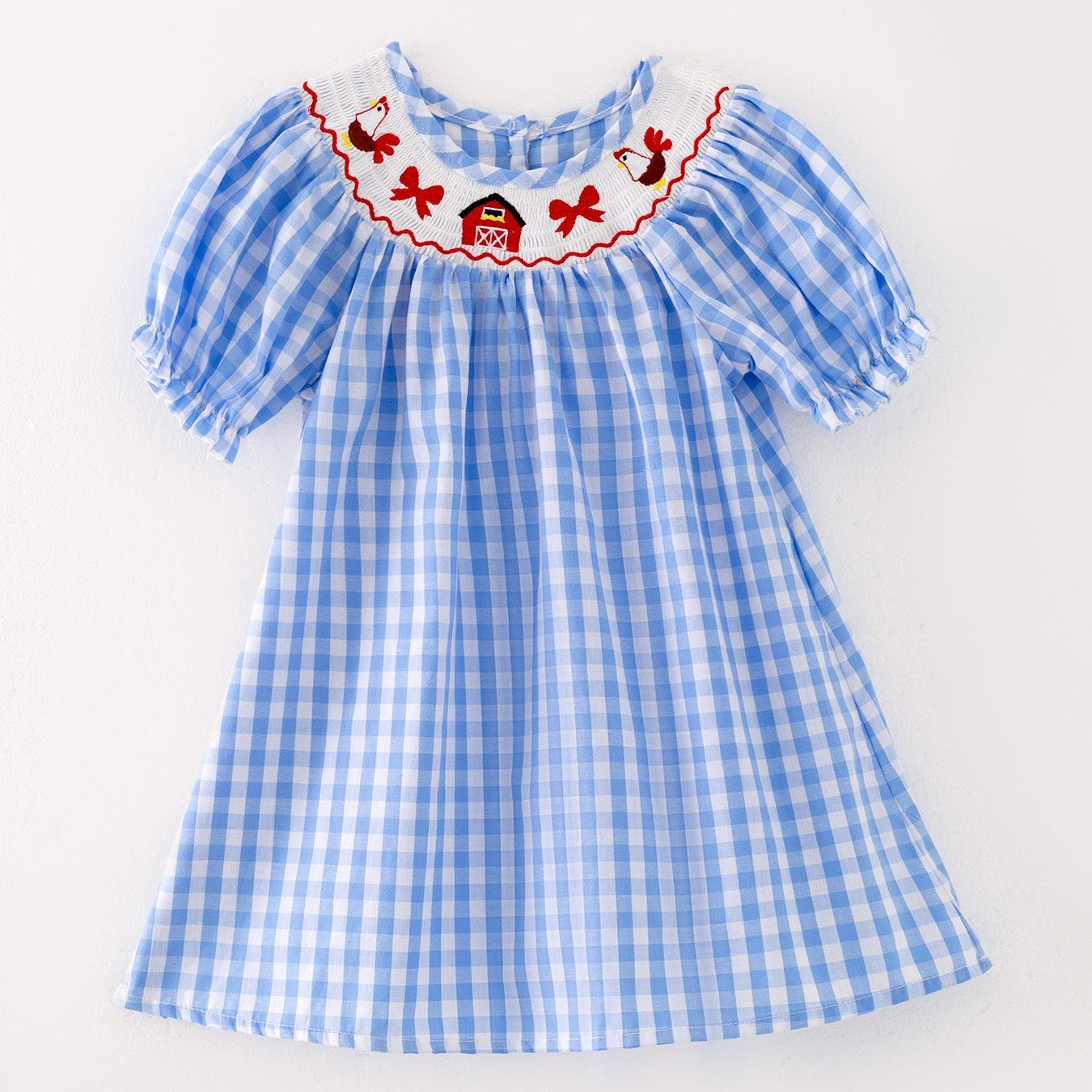 The front of a a blue checkered dress with red embroidered farm accents on a light gray background