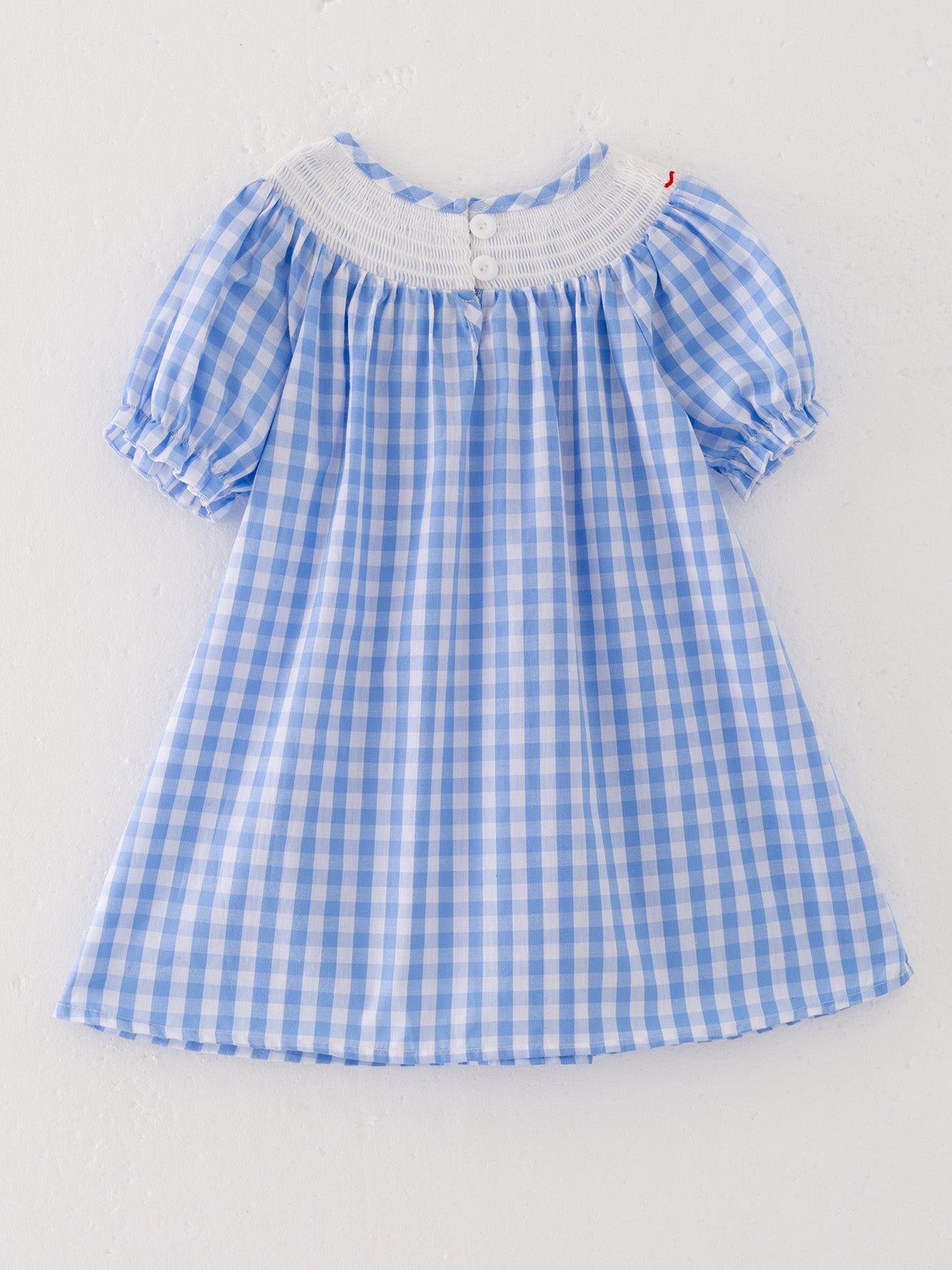 The back of a blue checkered dress with red embroidered farm accents on a light gray background