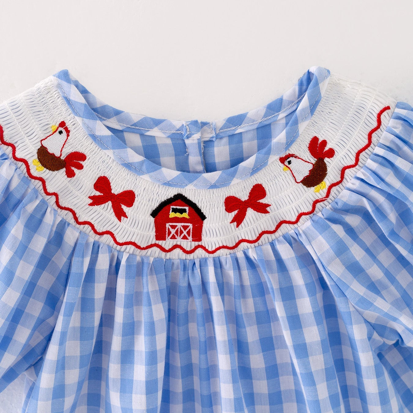 A close up of the front of a a blue checkered dress with red embroidered farm accents on a light gray background