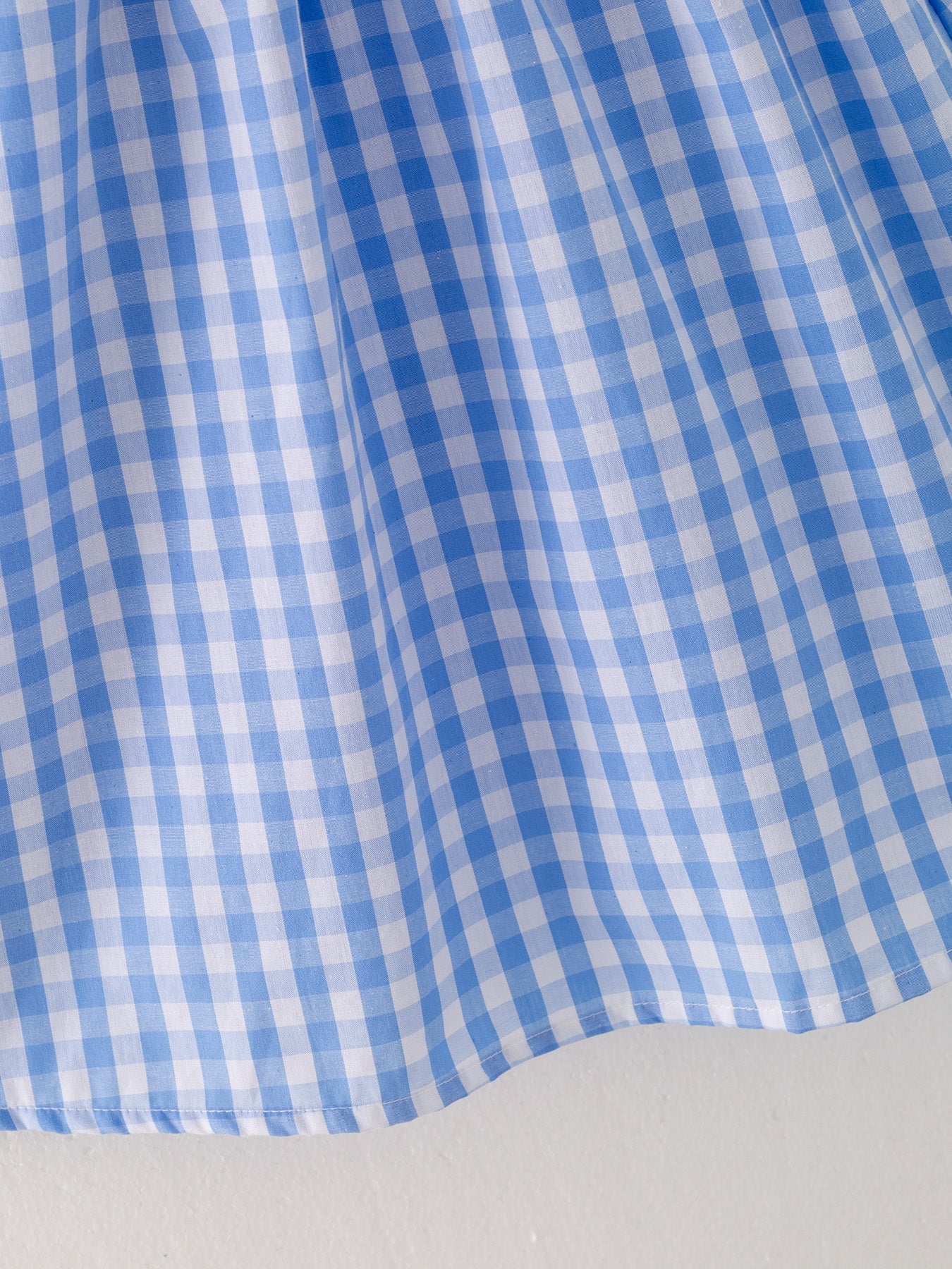 The hem of a a blue checkered dress with red embroidered farm accents on a light gray background