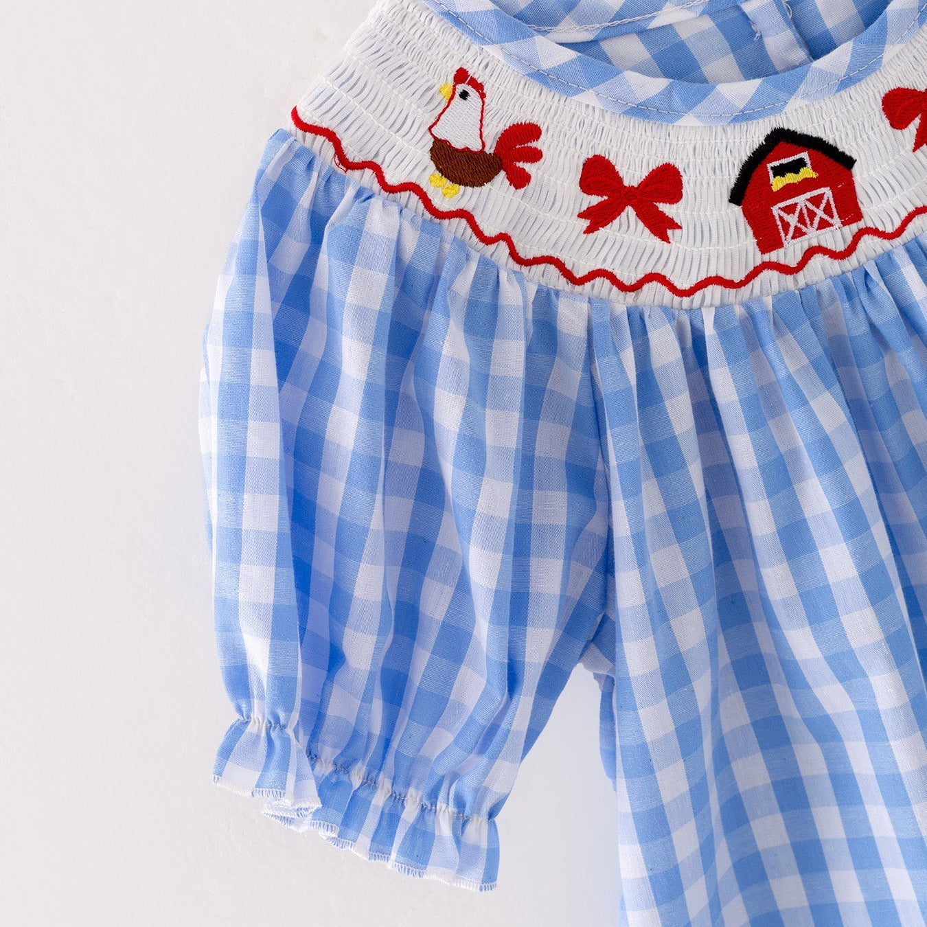The sleeve of a a blue checkered dress with red embroidered farm accents on a light gray background