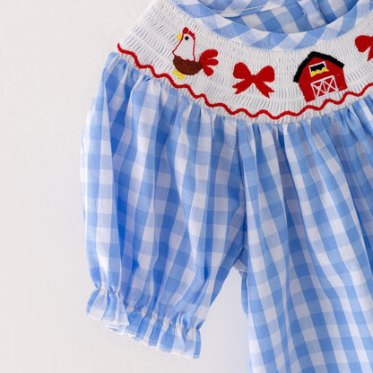 The sleeve of a a blue checkered dress with red embroidered farm accents on a light gray background
