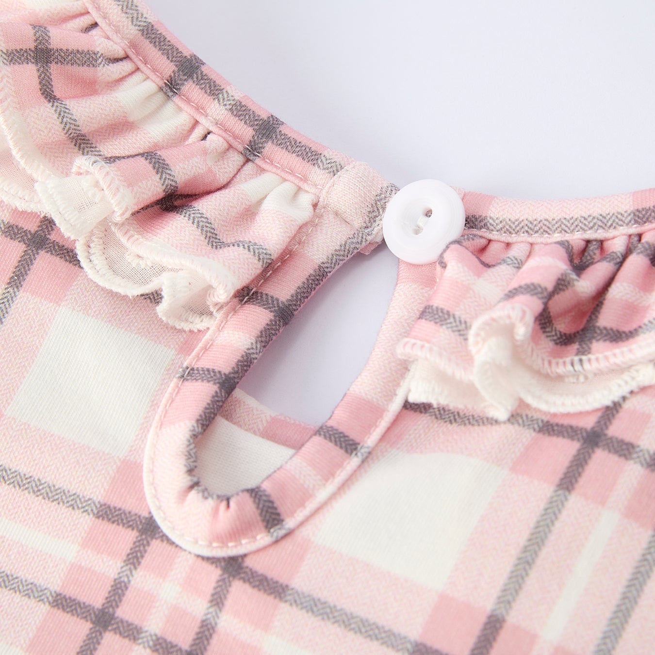 Back closure button of pink plaid dress with horse design on a hanger against a white background