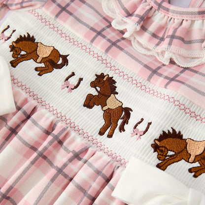 close up of embroidery on a pink plaid dress with horse design on a hanger against a white background