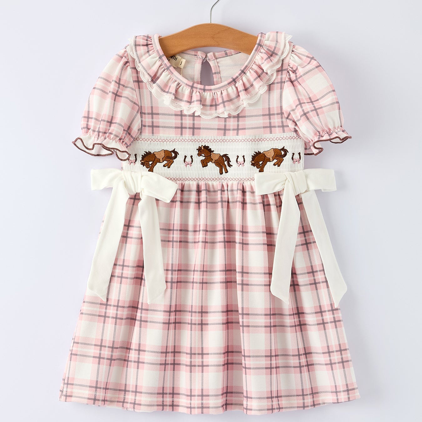 Pink plaid dress with horse design on a hanger against a white background