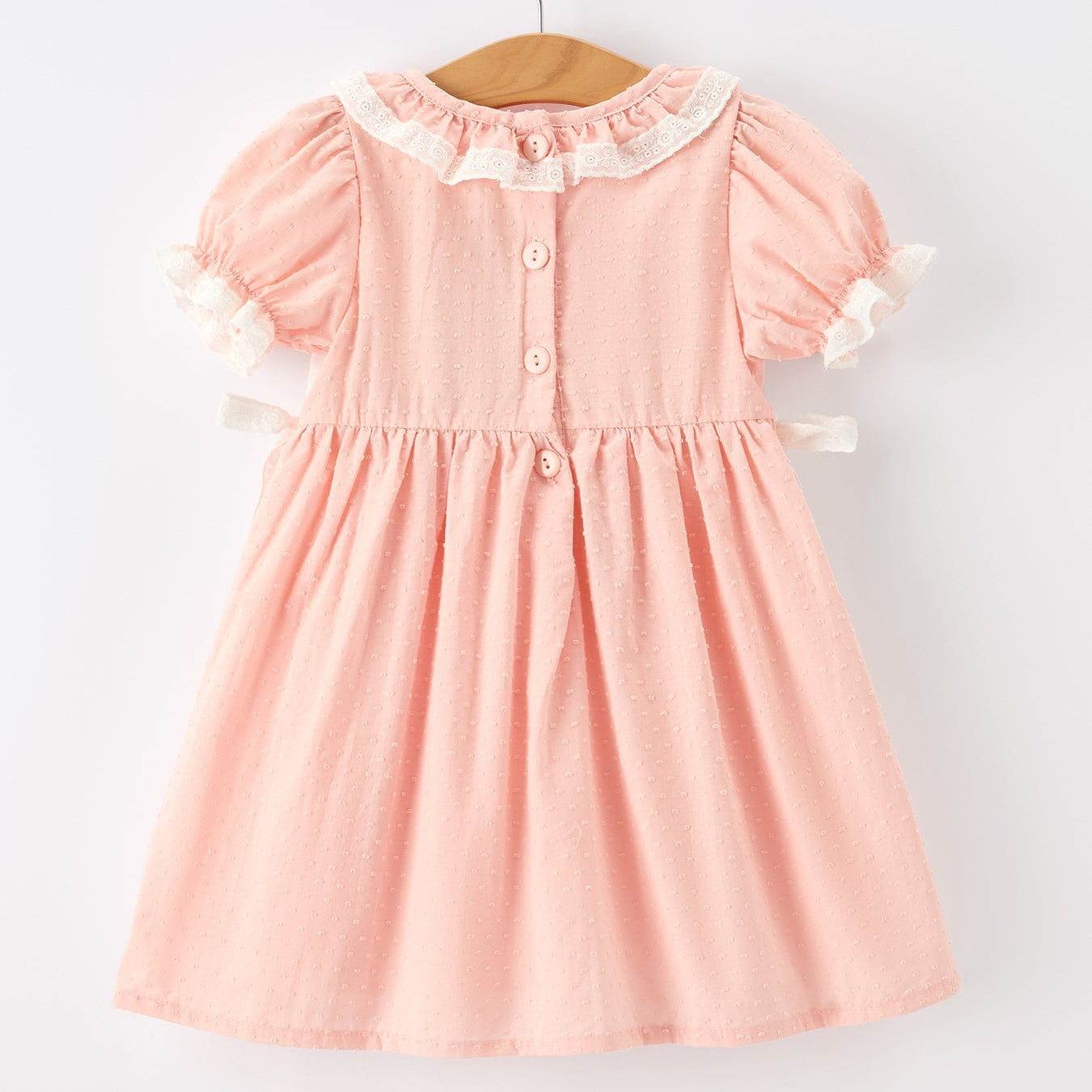 Back of pink dress with white collar and buttons on a hanger against a white background