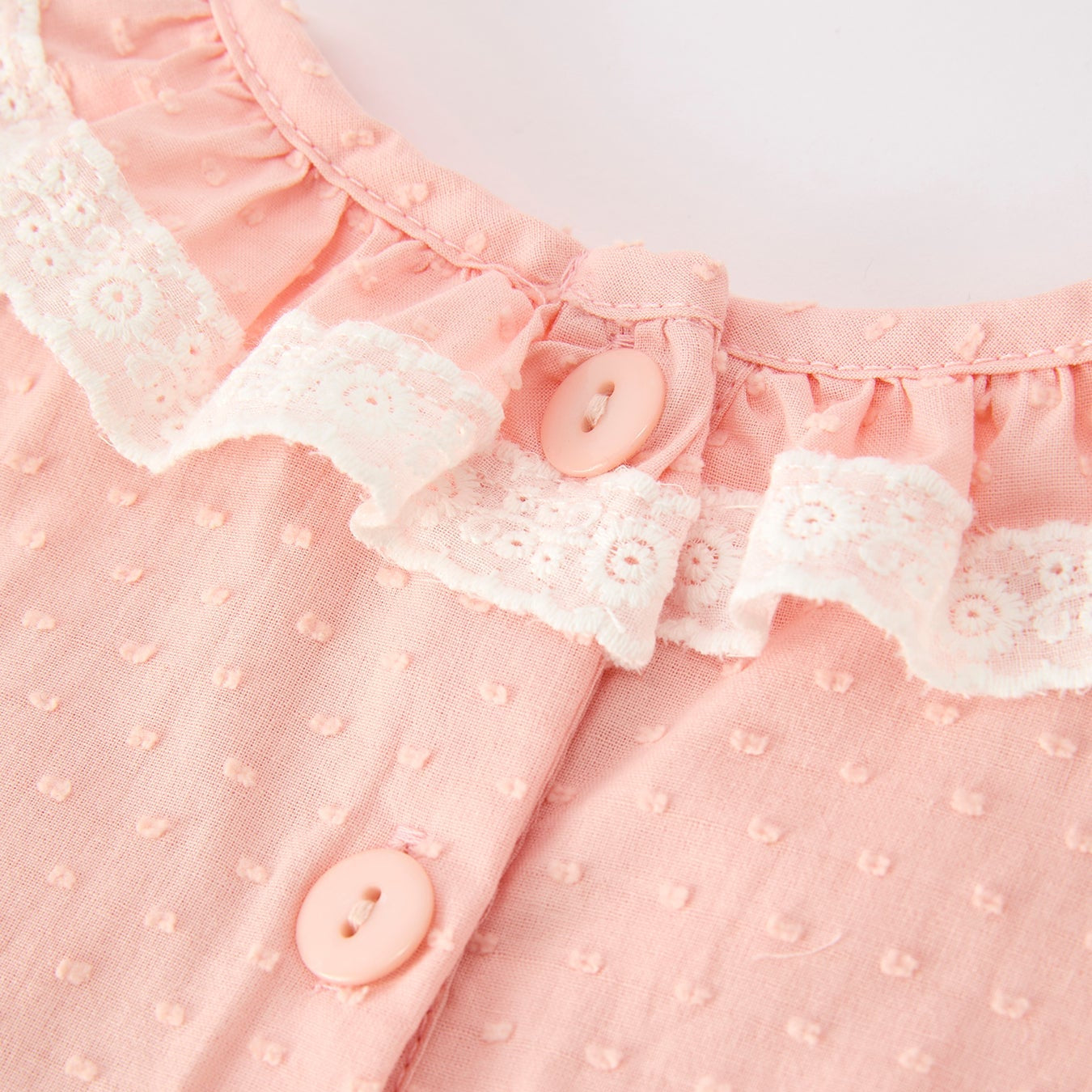 Close-up of a pink western horse dress with lace trim and buttons on a light background