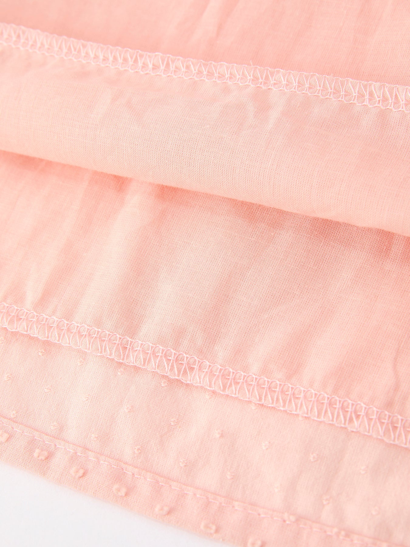Close-up of a pink fabric with lace trim on a white background