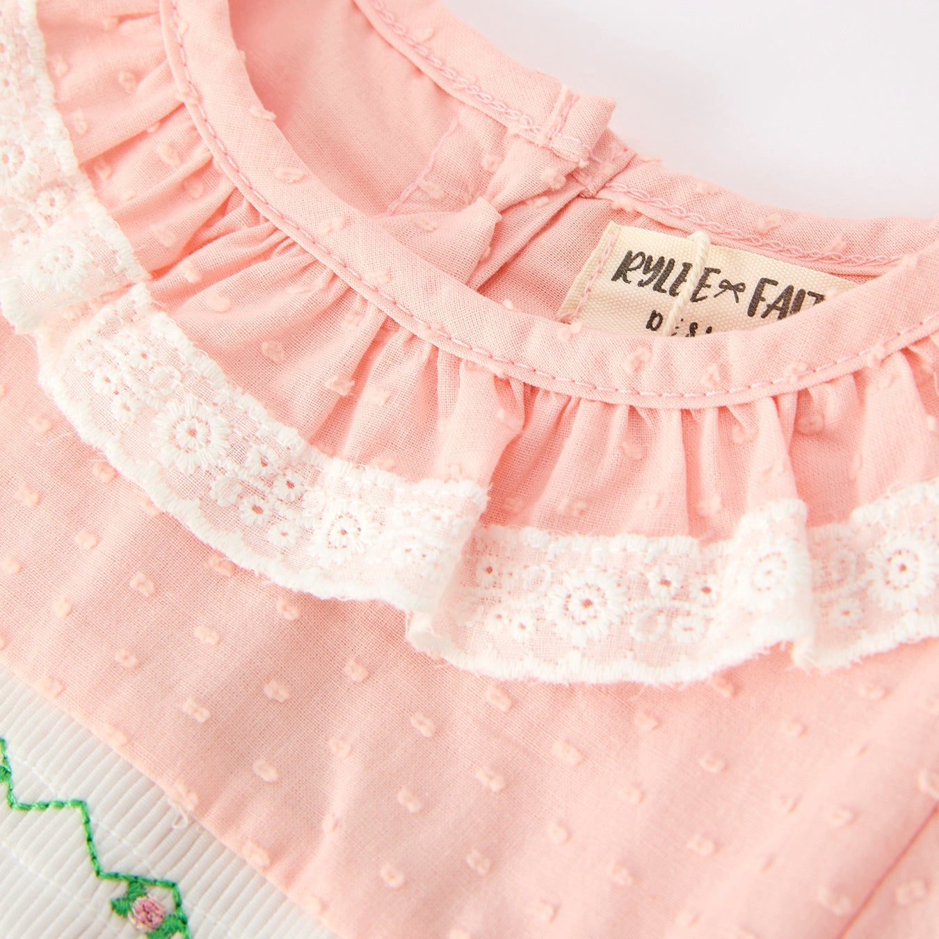 Close-up of a pink baby dress with lace details and a brand label.