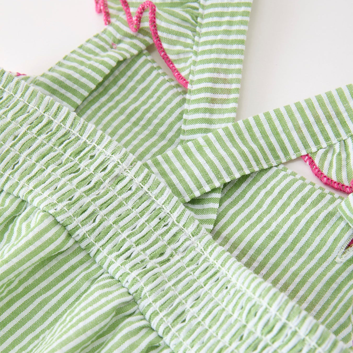 Close up of back straps on green striped western boots and cactus baby romper with pink accents on a white background