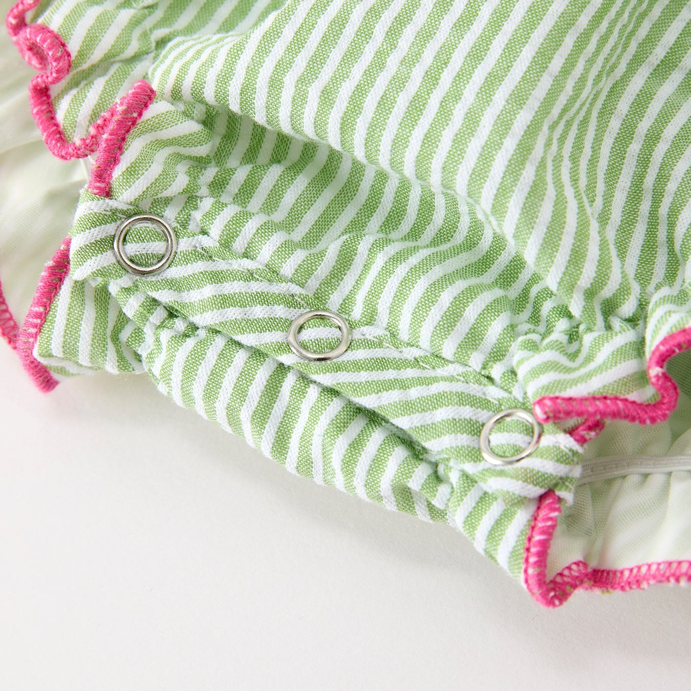 Close up of snaps on green striped western boots and cactus baby romper with pink accents on a white background