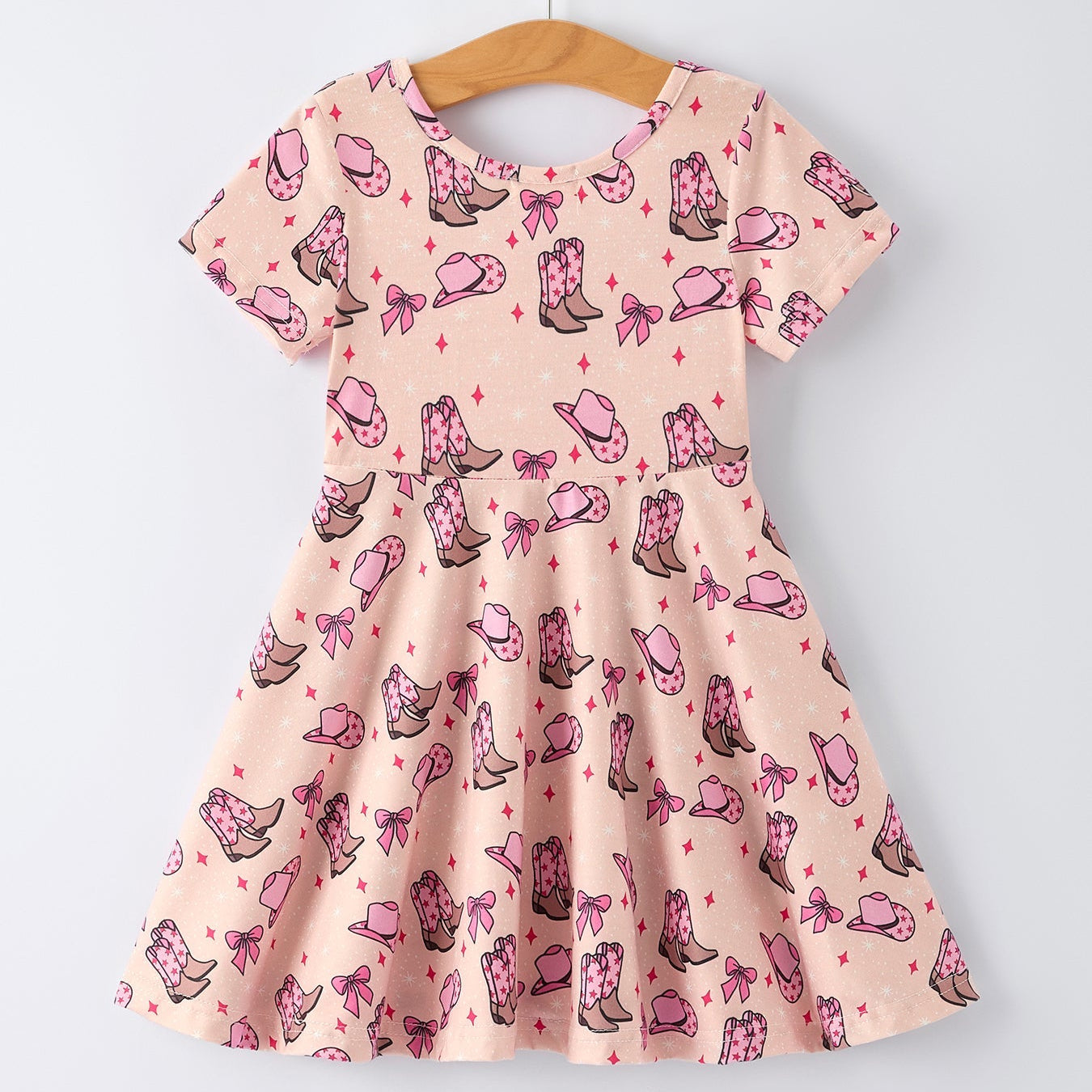 Pink dress with cowboy boot and bow pattern on a hanger against a white background