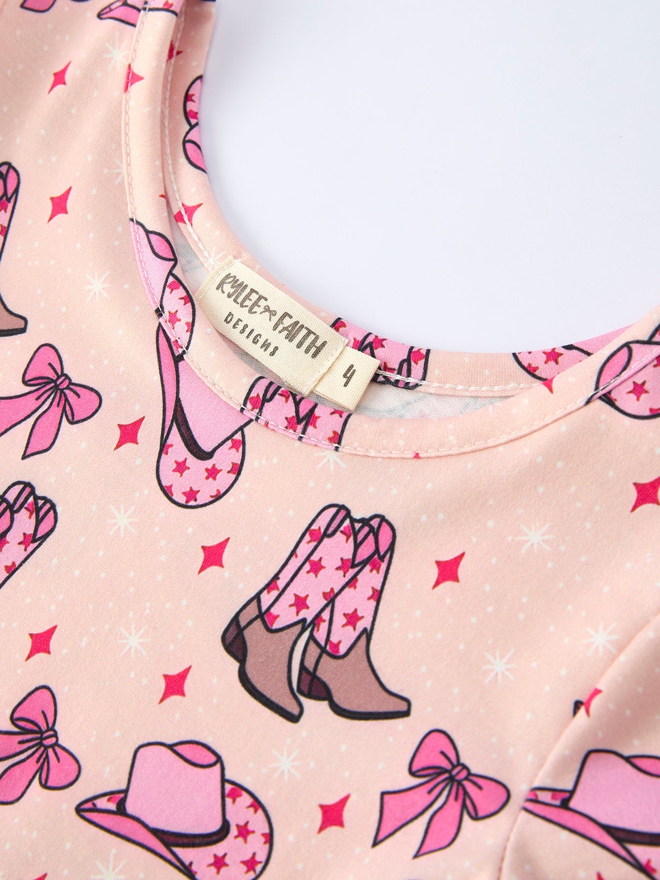 Pink shirt with cowboy boot, hat, and bow pattern, featuring a visible brand label.