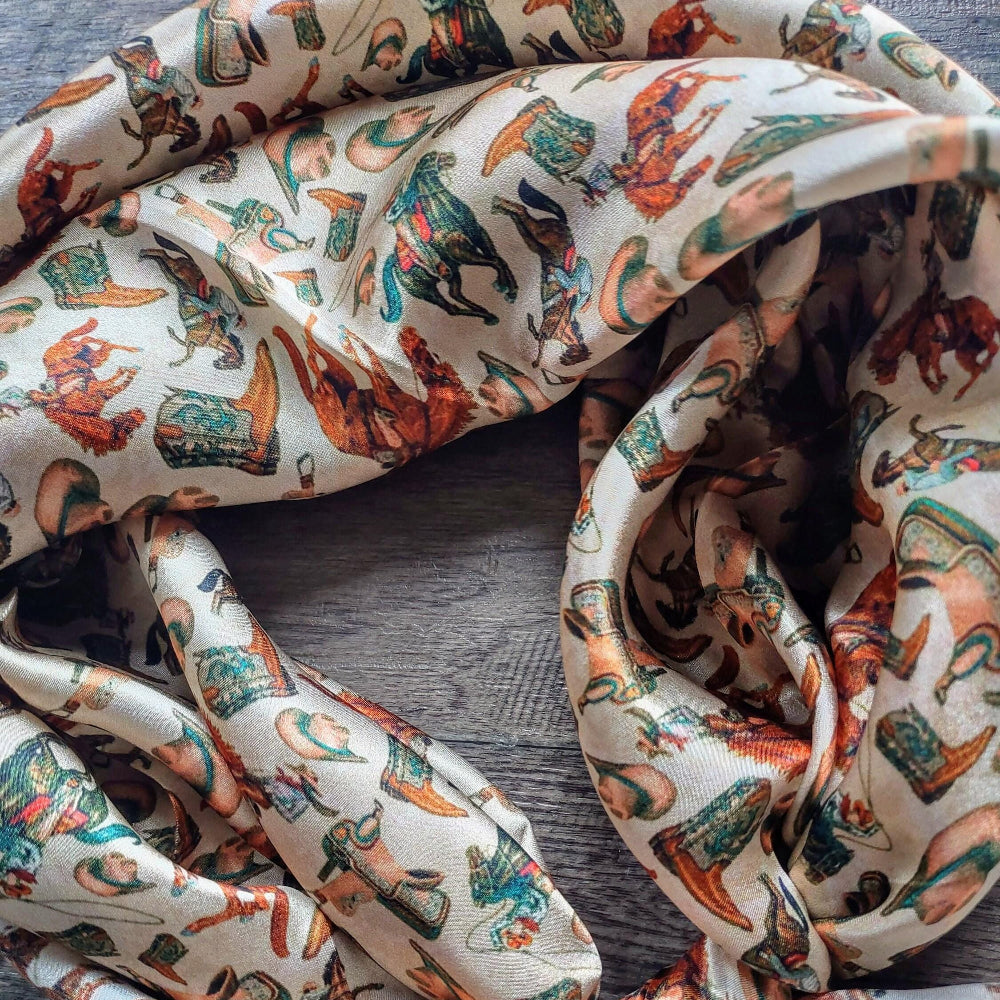 Close-up of Wild Rag 100% SILK Western Cowboy Western Neck Scarf Bandana Double B Wild Rags Western Boots, Hat, Cowgirl, Bucking Horse, Cowboy with browns and dark teal on a cream background.