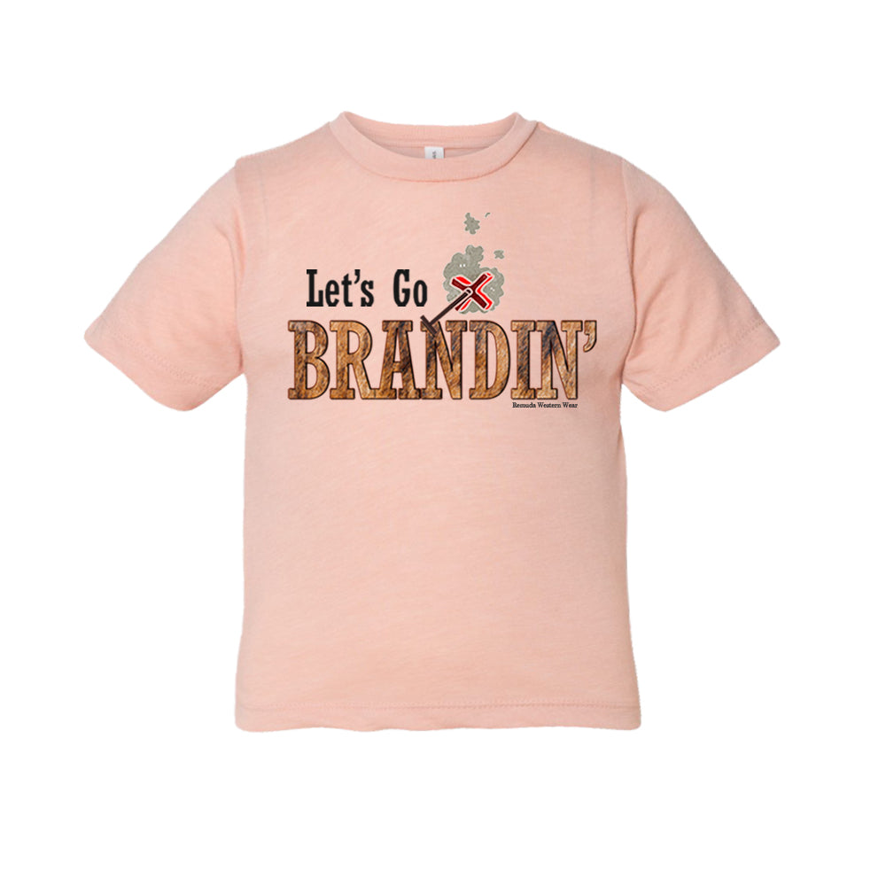 A stylish western-themed peach colored toddler t-shirt featuring the phrase 'Let's Go Brandin'' prominently printed in bold, weathered letters across the chest. Above the shirt is is an illustration of a branding iron, evoking a rustic cowboy aesthetic. Kids Western wear, Ranch wear and Rodeo wear.