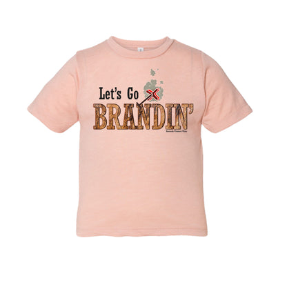 A stylish western-themed peach colored toddler t-shirt featuring the phrase 'Let's Go Brandin'' prominently printed in bold, weathered letters across the chest. Above the shirt is is an illustration of a branding iron, evoking a rustic cowboy aesthetic. Kids Western wear, Ranch wear and Rodeo wear.