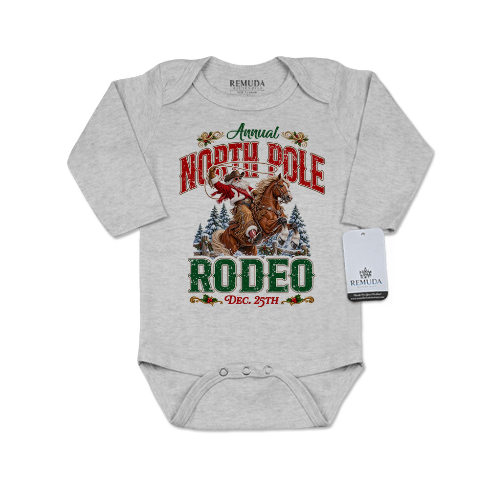 Heather Gray infant long sleeve Western Christmas romper featuring Cowboy Santa riding a rearing horse, festive North Pole Rodeo lettering in red and green, snowy pine trees, envelope-style shoulders, and snap closures for easy diaper changes.