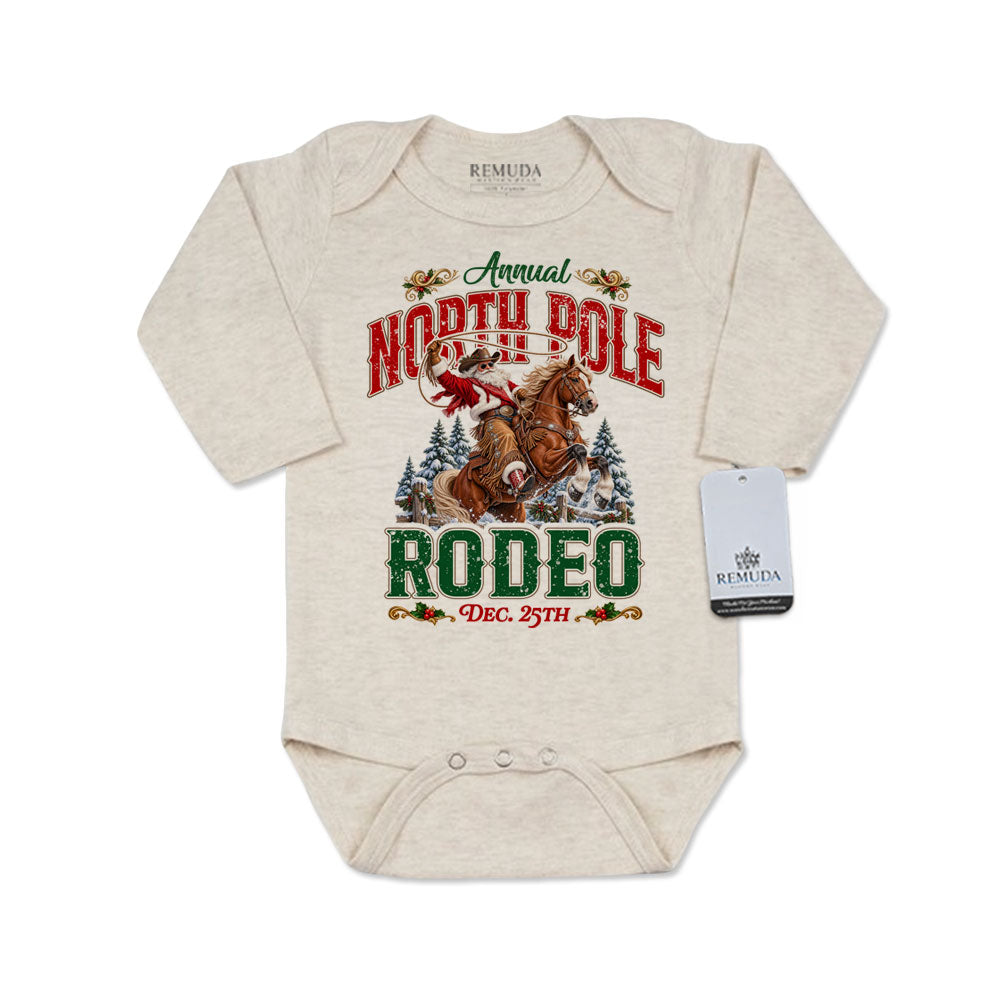 Oatmeal-colored infant long sleeve Western Christmas romper featuring Cowboy Santa riding a rearing horse, festive North Pole Rodeo lettering in red and green, snowy pine trees, envelope-style shoulders, and snap closures for easy diaper changes.