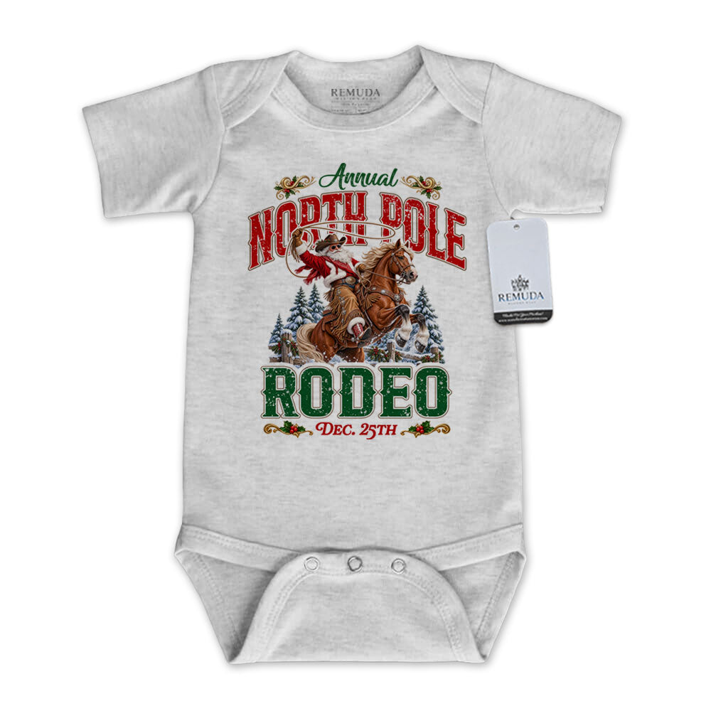 Heather Gray infant short sleeve Western Christmas romper featuring Cowboy Santa riding a rearing horse, festive North Pole Rodeo lettering in red and green, snowy pine trees, envelope-style shoulders, and snap closures for easy diaper changes.