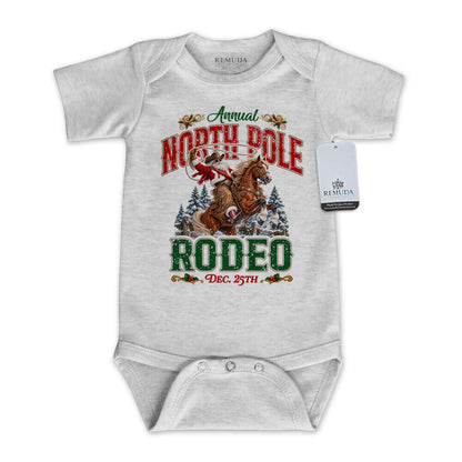 Heather Gray infant short sleeve Western Christmas romper featuring Cowboy Santa riding a rearing horse, festive North Pole Rodeo lettering in red and green, snowy pine trees, envelope-style shoulders, and snap closures for easy diaper changes.
