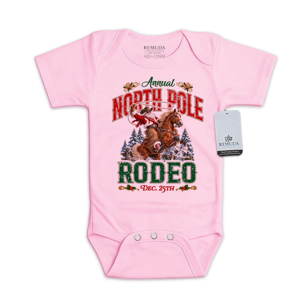 Pink infant short sleeve Western Christmas romper featuring Cowboy Santa riding a rearing horse, festive North Pole Rodeo lettering in red and green, snowy pine trees, envelope-style shoulders, and snap closures for easy diaper changes.