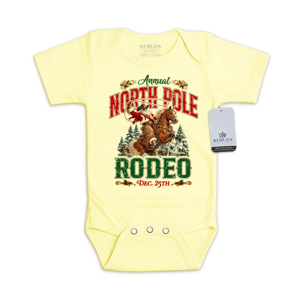 Yellow infant short sleeve Western Christmas romper featuring Cowboy Santa riding a rearing horse, festive North Pole Rodeo lettering in red and green, snowy pine trees, envelope-style shoulders, and snap closures for easy diaper changes.