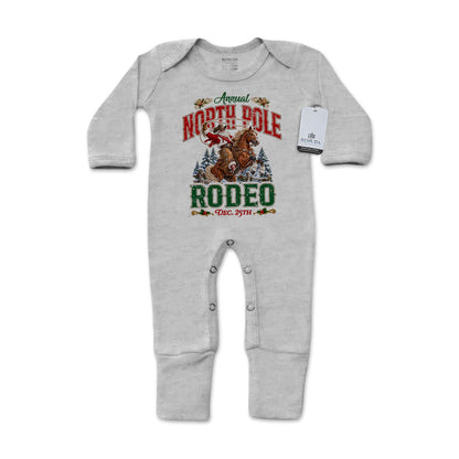 Heather Gray-colored infant one-piece footed pajamas featuring a festive North Pole Rodeo Christmas graphic with cowboy Santa riding a rearing horse, red and green lettering, long sleeves, and snap closures.