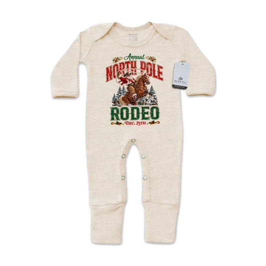 Oatmeal-colored infant one-piece footed pajamas featuring a festive North Pole Rodeo Christmas graphic with cowboy Santa riding a rearing horse, red and green lettering, long sleeves, and snap closures.