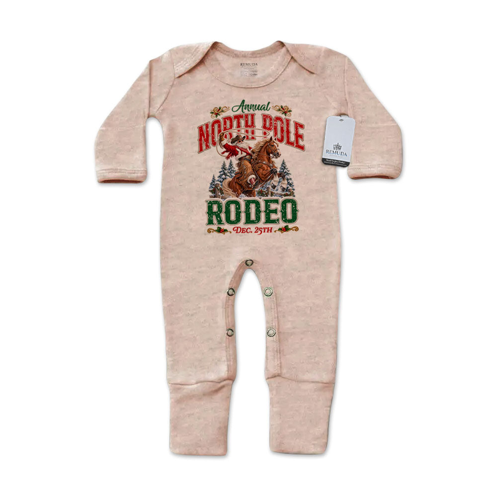 Sandstone-colored infant one-piece footed pajamas featuring a festive North Pole Rodeo Christmas graphic with cowboy Santa riding a rearing horse, red and green lettering, long sleeves, and snap closures.