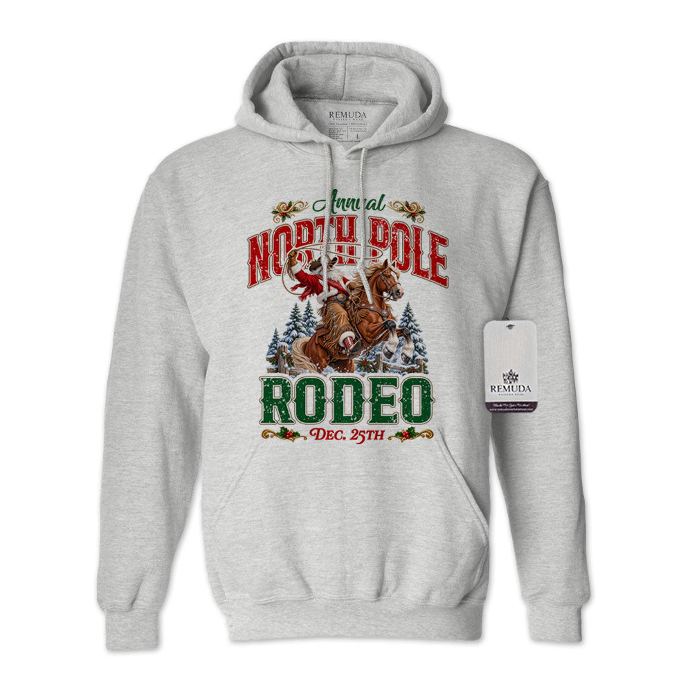 Ash Gray adult unisex pullover fleece hoodie featuring the Annual North Pole Rodeo Western Christmas design with Cowboy Santa riding a rearing horse, snowy pine trees, and festive red and green lettering reading “North Pole Rodeo – Dec. 25th.” Features a drawstring hood, kangaroo pocket, and ribbed cuffs and hem.