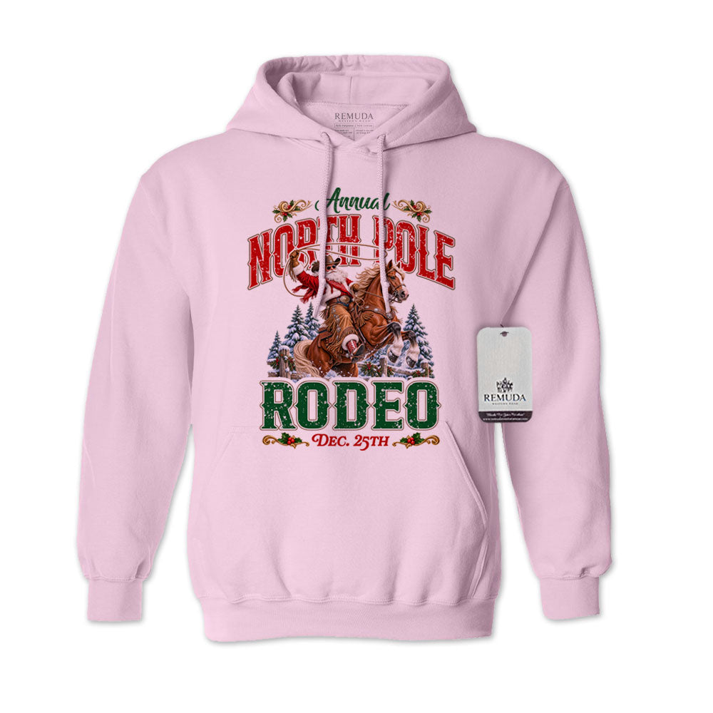 Light Pink adult unisex pullover fleece hoodie featuring the Annual North Pole Rodeo Western Christmas design with Cowboy Santa riding a rearing horse, snowy pine trees, and festive red and green lettering reading “North Pole Rodeo – Dec. 25th.” Features a drawstring hood, kangaroo pocket, and ribbed cuffs and hem.