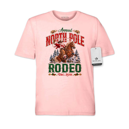 Light Pink adult unisex short sleeve T-shirt featuring a festive North Pole Rodeo Christmas design with Cowboy Santa riding a rearing horse, snowy pine trees, vintage red and green Western lettering, December 25th details, and a classic crewneck style.
