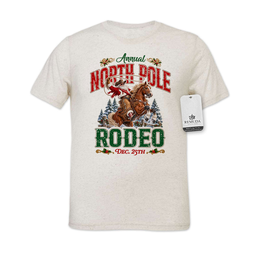 White fleckoatmeal-color shirt featuring a festive North Pole Rodeo Christmas design with Cowboy Santa riding a rearing horse, snowy pine trees, vintage red and green Western lettering, December 25th details, and a classic crewneck style.