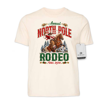 Solid Natural-color adult unisex short sleeve T-shirt featuring a festive North Pole Rodeo Christmas design with Cowboy Santa riding a rearing horse, snowy pine trees, vintage red and green Western lettering, December 25th details, and a classic crewneck style.