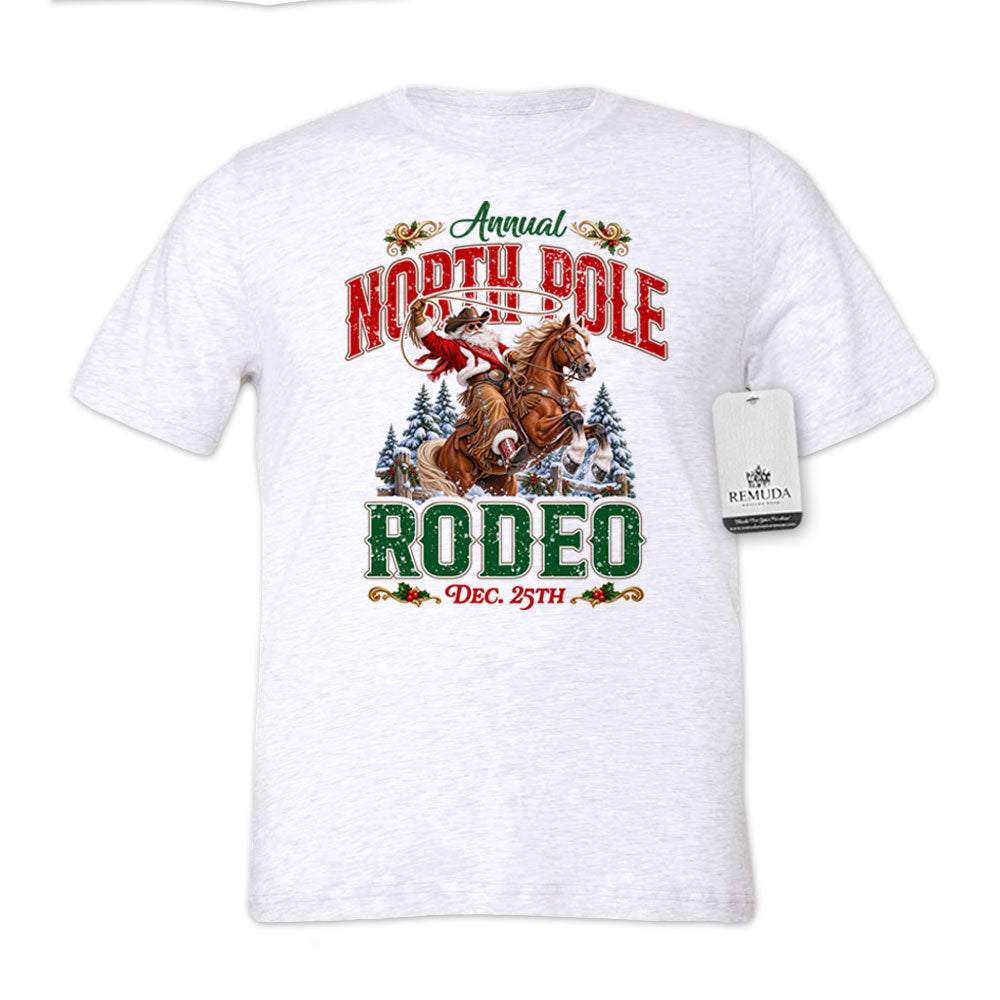 White fleck adult unisex short sleeve T-shirt featuring a festive North Pole Rodeo Christmas design with Cowboy Santa riding a rearing horse, snowy pine trees, vintage red and green Western lettering, December 25th details, and a classic crewneck style.