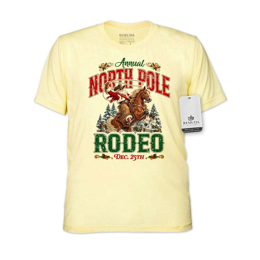 Light Yellow adult unisex short sleeve T-shirt featuring a festive North Pole Rodeo Christmas design with Cowboy Santa riding a rearing horse, snowy pine trees, vintage red and green Western lettering, December 25th details, and a classic crewneck style.