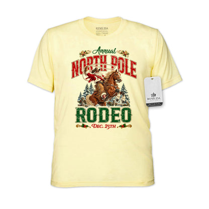 Light Yellow adult unisex short sleeve T-shirt featuring a festive North Pole Rodeo Christmas design with Cowboy Santa riding a rearing horse, snowy pine trees, vintage red and green Western lettering, December 25th details, and a classic crewneck style.