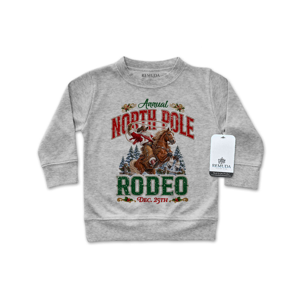 Heather gray infant long sleeve pullover sweatshirt featuring a festive North Pole Rodeo Christmas design with Cowboy Santa riding a rearing horse, snowy pine trees, vintage red and green lettering, and ribbed cuffs and hem.