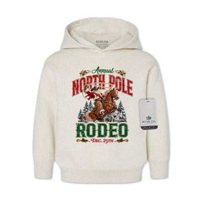 Oatmeal-colored toddler pullover hoodie featuring a festive North Pole Rodeo Christmas design with Cowboy Santa riding a rearing horse, snowy pine trees, vintage red and green lettering, December 25th details, and ribbed cuffs and hem.